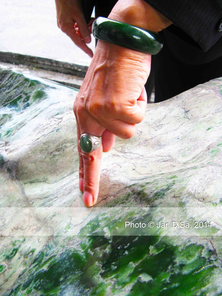 This lady is wearing a green jade bangle, a green jade ring and gestures to a huge green jade boulder.